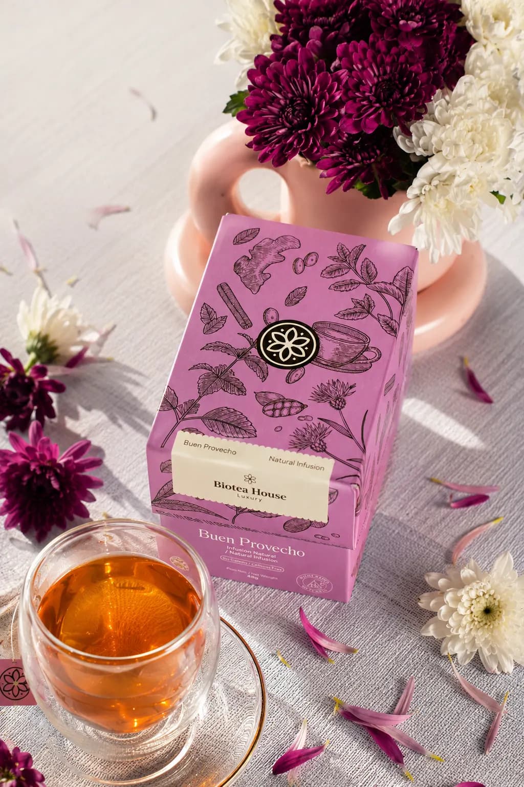 Caja de Buen Provecho rodeada de flores silvestres moradas y blancas con una taza de te infusionado de color ambar dorado.