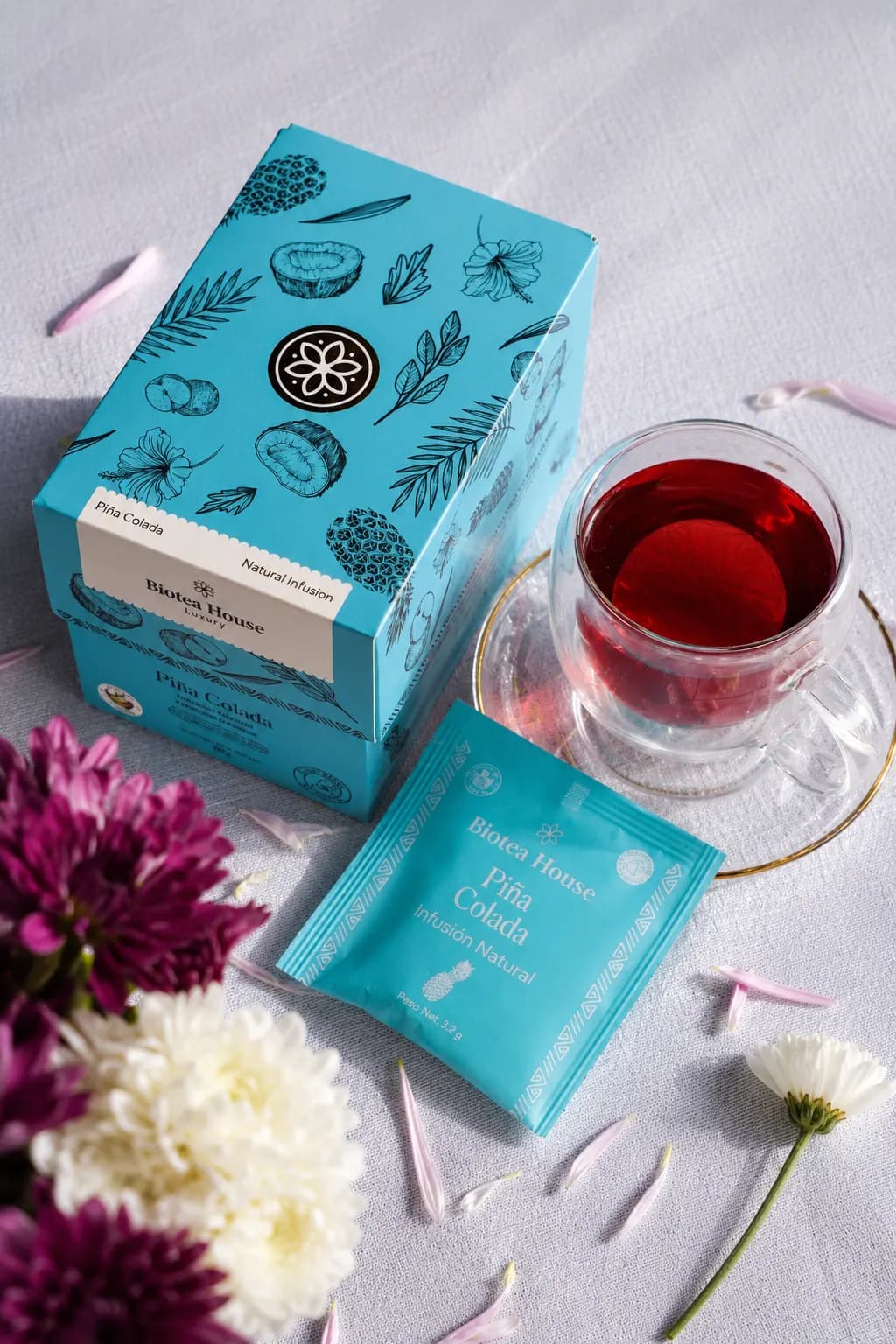 Escena de Biotea House con cajas de té de colores, una taza de té rojo y flores frescas alrededor.